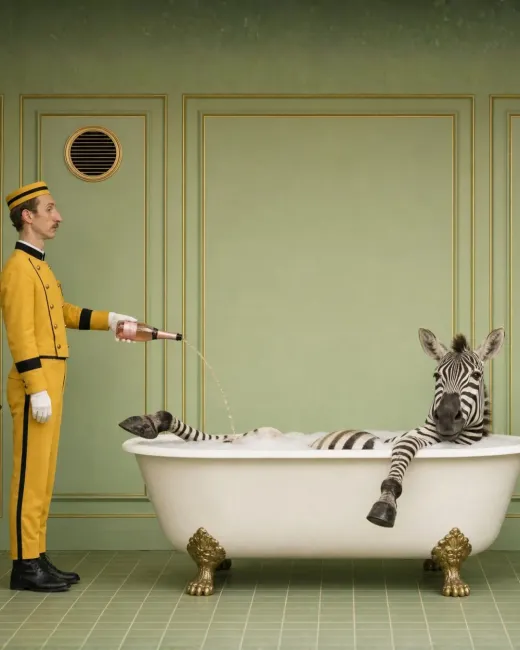 Page schenkt einem Zebra in einer Badewanne Champagner ein