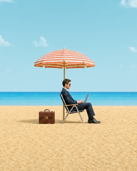 Mann im Anzug arbeitet mit einem Laptop unter einem Sonnenschirm am Meer